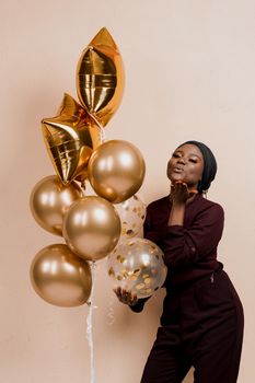 Black girl with golden ballons have a party and send a kiss. African woman celebrate new year. Happy emotions of muslim young woman