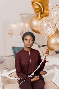 Black girl with golden ballons have a party and smiles. African woman celebrate graduation. Happy emotions of muslim young woman
