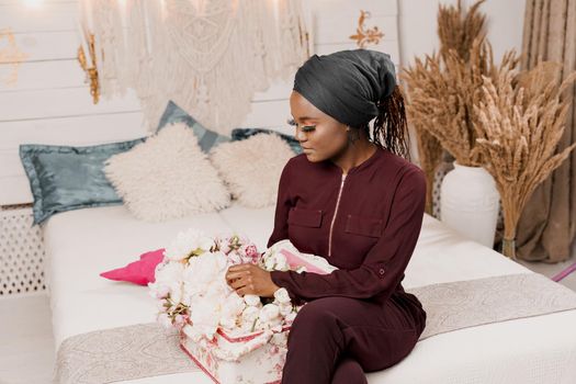 Muslim girl with flowers seats and looks at bouquet. African young woman with beautiful flowers from her boyfriend on the valentines day. Holiday celebration