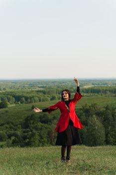 Georgian woman dances national dance in red national dress on the green hills of Georgia background. Georgian culture lifestyle.