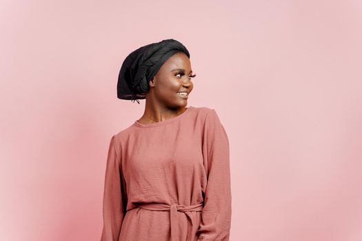 Muslim young woman weared in traditional dress and scarf isolated on pink background. Attractive and confident black model in studio