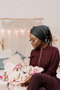 Muslim girl with flowers seats and looks at bouquet. African young woman with beautiful flowers from her boyfriend on the valentines day. Holiday celebration