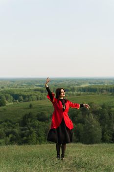 Georgian woman dances national dance in red national dress on the green hills of Georgia background. Georgian culture lifestyle.