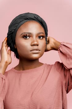 Muslim woman close-up. Relax and meditation. African black attractive girl vertical portrait isolated on pink background