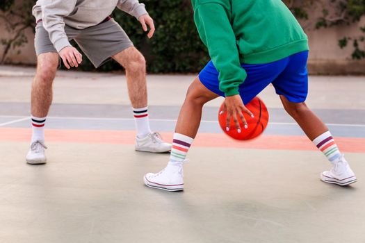 legs of two unrecognizable friends playing basketball on a city court, concept of urban sport in the street