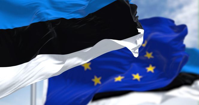 Detail of the national flag of Estonia waving in the wind with blurred european union flag in the background on a clear day. Democracy and politics. European country. Selective focus.