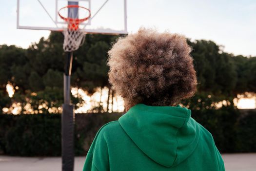 rear view of an unrecognizable person on the basketball court of a city park, concept of urban sport in the street, copy space for text