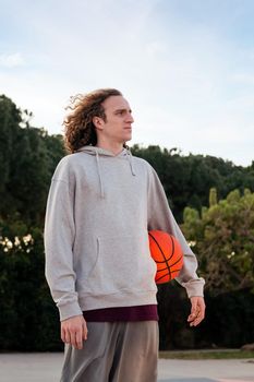 caucasian man outdoors with a basketball under his arm, concept of urban sport in the street, copy space for text