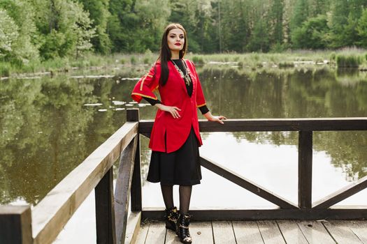 Georgian woman in red national dress with cross symbols. Attractive woman on the lake. Georgian culture lifestyle. Woman looks into camera