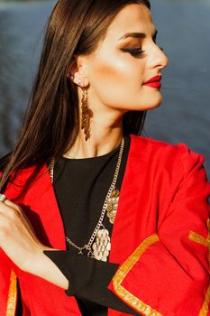 Georgian girl in red national dress with cross symbols. Attractive woman on the lake. Georgian culture lifestyle. Woman looks right side