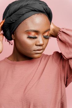 Muslim woman with closed eyes close-up. Relax and meditation. African black attractive girl vertical portrait isolated on pink background