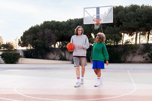 couple of friends chatting while walking on the basketball court after training, concept of friendship and urban sport in the street, copy space for text