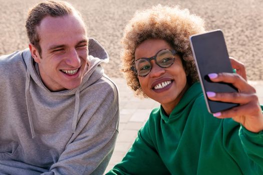young latin woman and caucasian man smiling while taking a selfie photo with the mobile phone, concept of lifestyle and friendship
