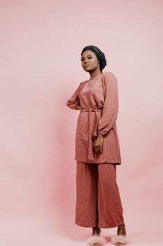 Muslim young woman weared in traditional dress and scarf isolated on pink background. Attractive and confident black model in studio