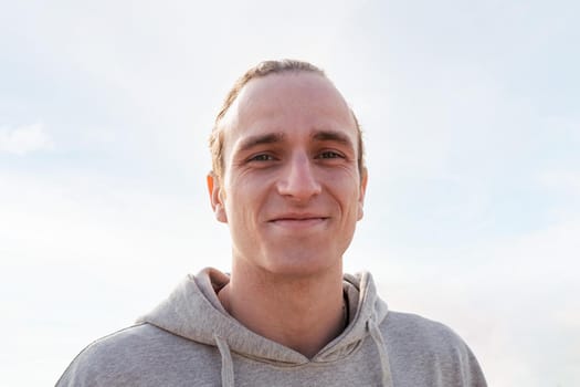 portrait of a young caucasian man smiling happy and looking at camera with sky in background, concept of happiness and lifestyle, copy space for text
