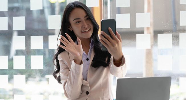 Businesswoman video call with clients on smartphone waving at screen..