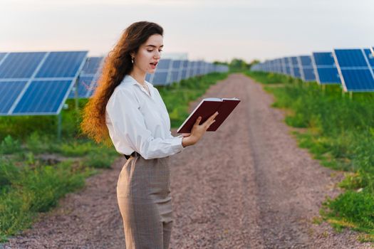 Attractive girl stand and read book near solar panels row on the ground. Woman investor wears formal white shirt
