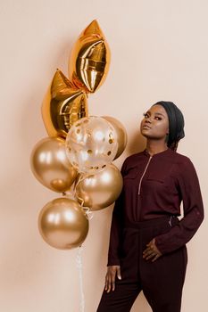 Muslim black girl with golden helium balloons isolated peach background. African young woman celebrates her birthday