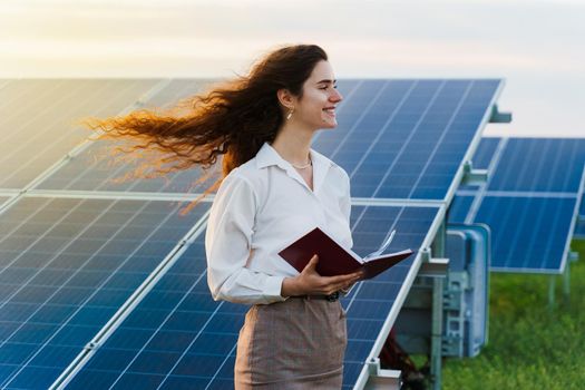 Model with solar panels stands in row on the ground. Girl dressed white formal shirt smiles on the power plant