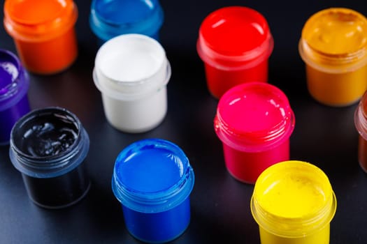 full-frame close-up background of opened small gouache paint jars on flat black surface