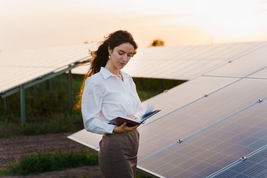 Girl and solar panels stands in row on the ground at sunset. Solar cells power plant business