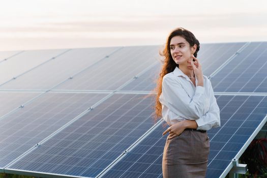 Model with solar panels stands in row on the ground. Girl dressed white formal shirt smiles on the power plant