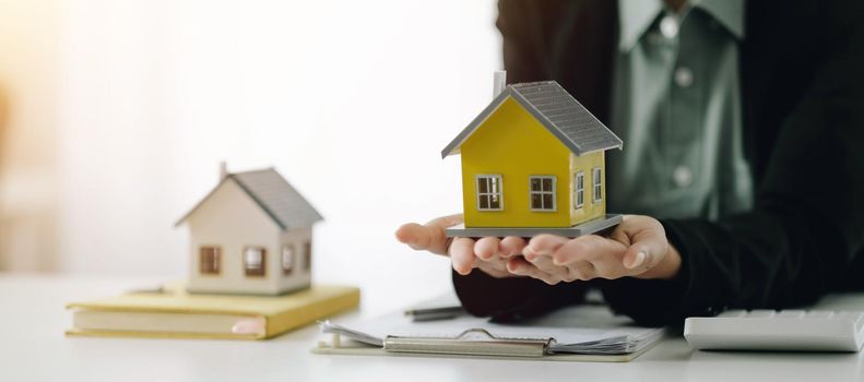 Miniature house in the hands of an Asian woman real estate agent home loan working at the office. Looking at the camera..