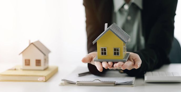 Miniature house in the hands of an Asian woman real estate agent home loan working at the office. Looking at the camera..