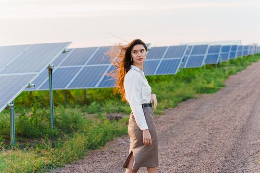 Girl stand between 2 Solar panels row on the ground at sunset. Free electricity for home. Sustainability of planet