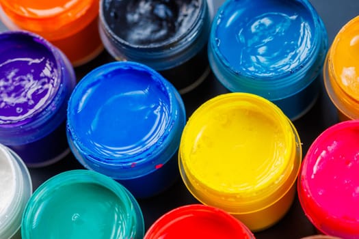 full-frame close-up background of opened small gouache paint jars on black