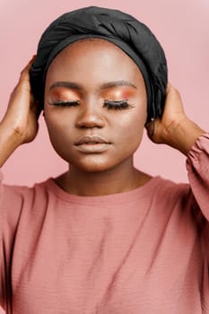 Muslim woman with closed eyes close-up. Relax and meditation. African black attractive girl vertical portrait isolated on pink background