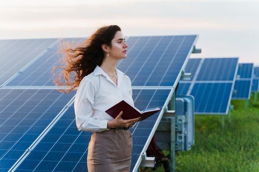 Model with solar panels stands in row on the ground. Girl dressed white formal shirt smiles on the power plant