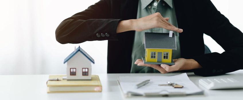 Miniature house in the hands of an Asian woman real estate agent home loan working at the office.