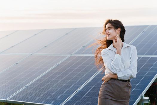 Model with solar panels stands in row on the ground. Girl dressed white formal shirt smiles on the power plant