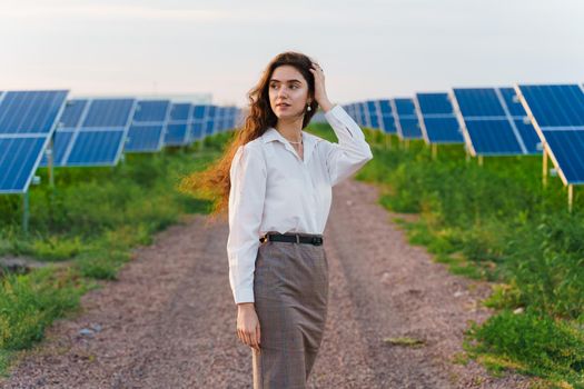 Girl stand between 2 Solar panels row on the ground at sunset. Free electricity for home. Sustainability of planet