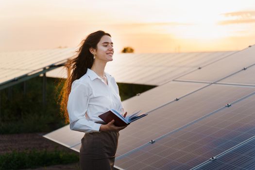Girl and solar panels stands in row on the ground at sunset. Solar cells power plant business