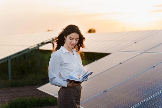 Girl and solar panels stands in row on the ground at sunset. Solar cells power plant business