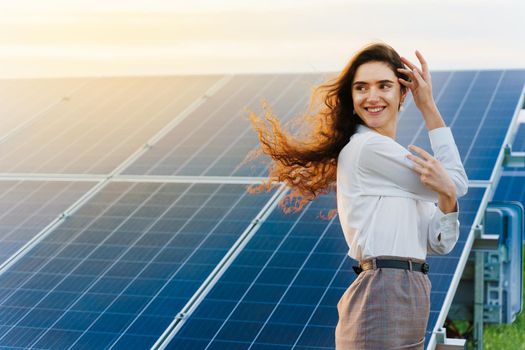 Model with solar panels stands in row on the ground. Girl dressed white formal shirt smiles on the power plant