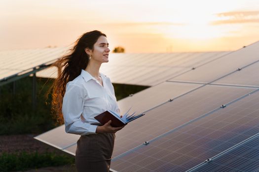 Girl and solar panels stands in row on the ground at sunset. Solar cells power plant business