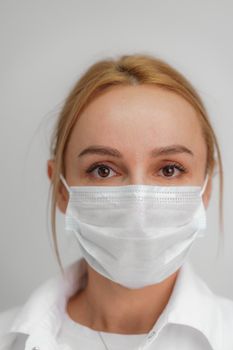 Close-up portrait of a young blonde woman in a medical mask on a light background. Virus protection. Coronovirus covid-19 The concept of a pandemic epidemic. Quarantine. Stay at home
