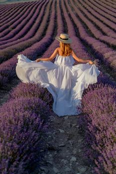 charming Young woman with a hat and white dress in a purple lavender field. LIfestyle outdoors. Back view.