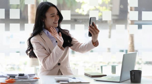Businesswoman video call with clients on smartphone waving at screen.