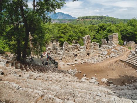 PHASELIS, TURKEY - May 19, 2018. Tourists walk into ruins of amphitheatre of ancient Phaselis city. Panorama view on famous architectural landmark, Kemer district, Antalya province.