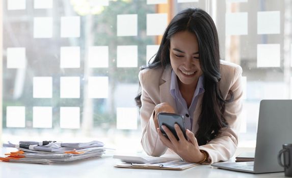 Beautiful asian woman happy to play on the phone at desk office..