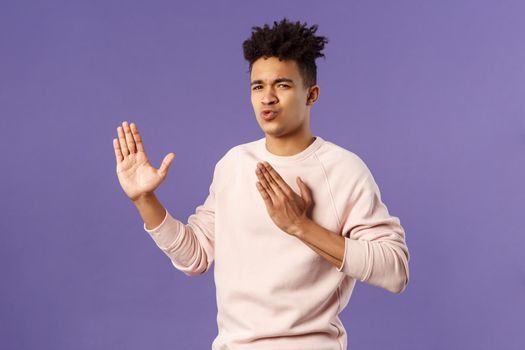 Portrait of funny and carefree young hispanic guy holding hands in martial arts attack pose, folding lips acting sassy and cool as imitating ninja, ready to defeat coronavirus, purple background.