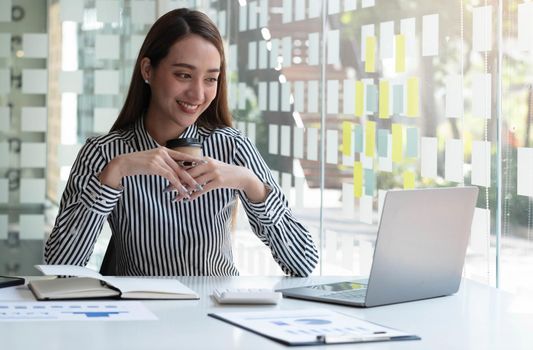 Smiling Asian businesswoman holding a coffee mug and laptop at the office.