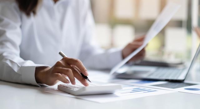 Close up Business woman using calculator and laptop for do math finance on wooden desk in office and business working background, tax, accounting, statistics and analytic research concept.