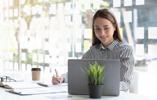 Charming asian businesswoman sitting working on laptop in office..