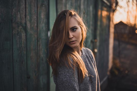 beautiful young blonde model girl. White pants. gray knitted sweater. black boots. wooden pendant on the neck in the form of a horse. On the Sunset. Portrait.