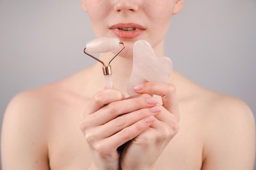 Caucasian woman holding pink roller massager and gouache scraper on white background